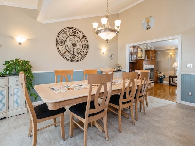dining space featuring wainscoting, crown molding, a tile fireplace, and an inviting chandelier