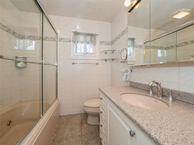 full bathroom featuring vanity, tile walls, toilet, and combined bath / shower with glass door