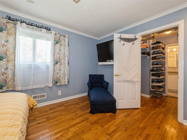 bedroom featuring wood-type flooring, crown molding, visible vents, baseboards, and a spacious closet