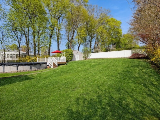 view of yard featuring a fenced backyard, an outbuilding, a covered pool, a deck, and a storage shed