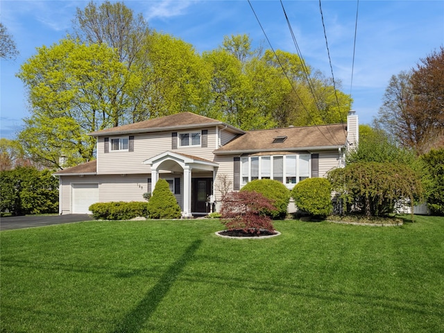 split level home with a garage, a chimney, a front yard, and aphalt driveway
