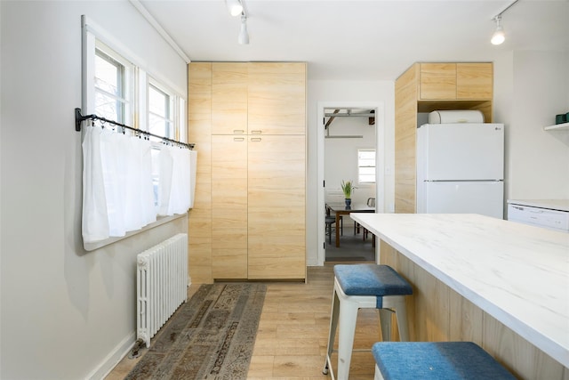 kitchen with radiator heating unit, light brown cabinetry, a kitchen breakfast bar, rail lighting, and freestanding refrigerator