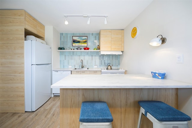 kitchen with a breakfast bar, white appliances, light wood-style flooring, rail lighting, and a peninsula