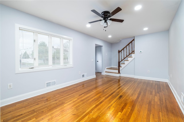 unfurnished living room featuring hardwood / wood-style flooring, a ceiling fan, visible vents, and stairway