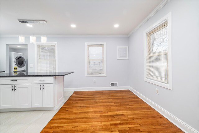 kitchen featuring stacked washer / dryer, a wealth of natural light, white cabinetry, decorative light fixtures, and ornamental molding
