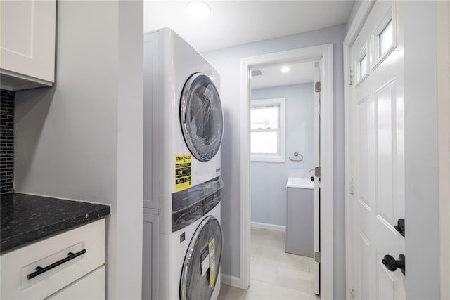 laundry area featuring light tile patterned flooring, stacked washing maching and dryer, cabinet space, baseboards, and recessed lighting