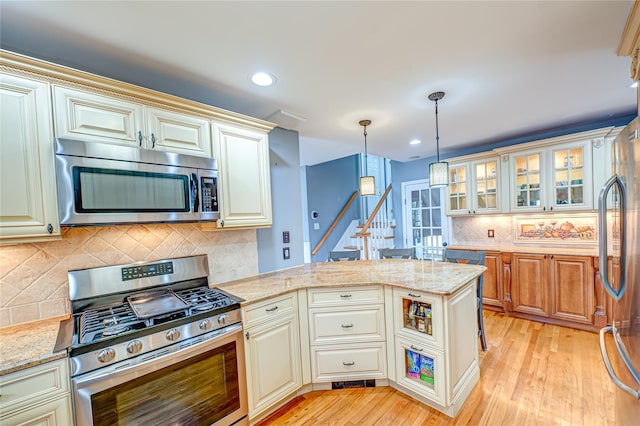 kitchen featuring stainless steel appliances, a peninsula, light wood-style floors, backsplash, and decorative light fixtures