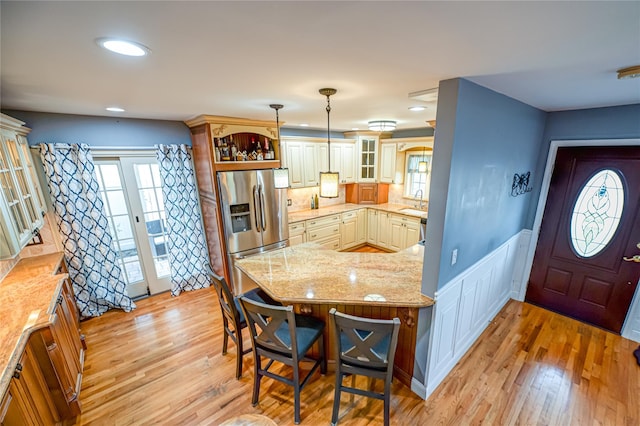 kitchen featuring stainless steel refrigerator with ice dispenser, light wood-style floors, glass insert cabinets, and light stone counters