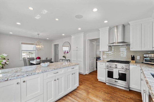 kitchen featuring high end range, recessed lighting, white cabinets, and wall chimney exhaust hood
