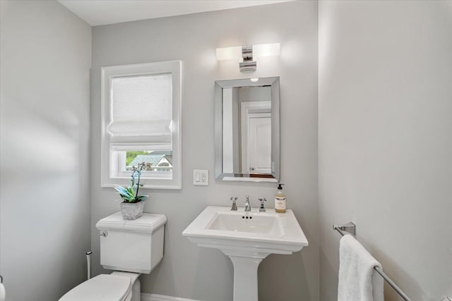 half bathroom with baseboards, toilet, and a sink