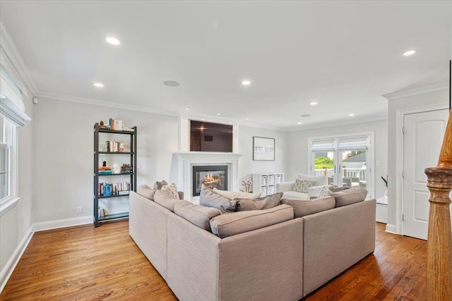 living area with crown molding, a glass covered fireplace, recessed lighting, and light wood-type flooring
