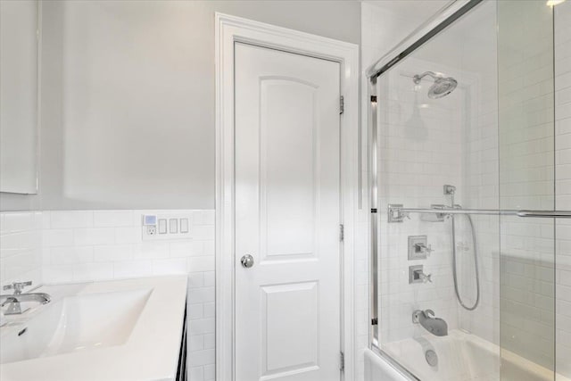 full bathroom featuring tile walls, bath / shower combo with glass door, and a sink
