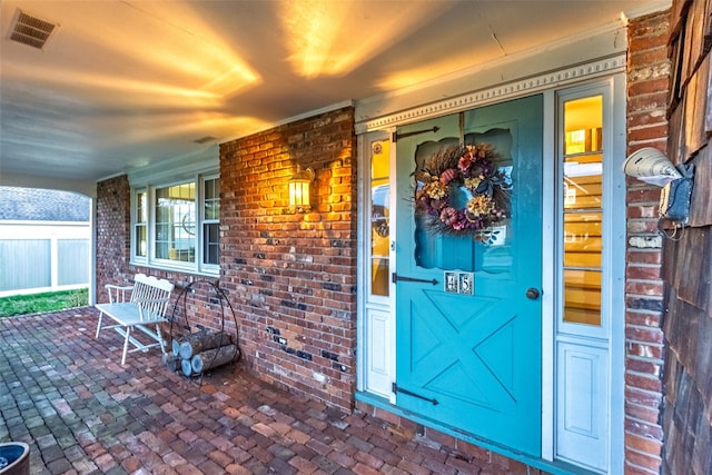 entrance to property featuring visible vents, a porch, and brick siding