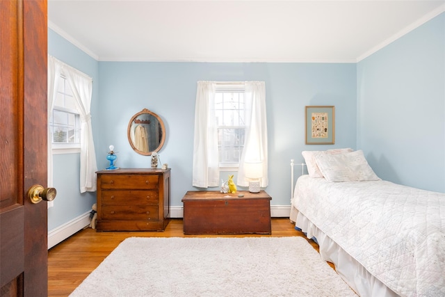 bedroom with wood finished floors, ornamental molding, and a baseboard heating unit