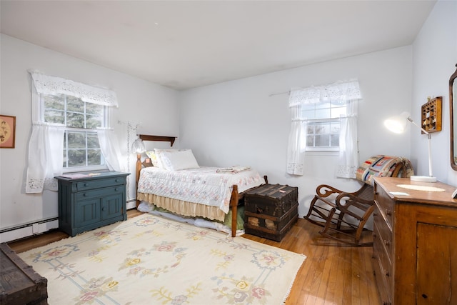 bedroom with light wood-style flooring, a baseboard heating unit, and multiple windows