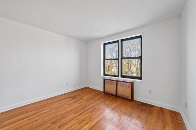 spare room featuring radiator heating unit, light wood-style flooring, and baseboards