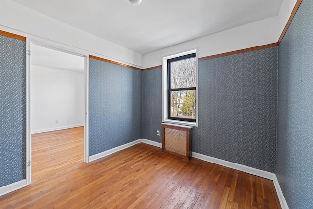 empty room featuring wood-type flooring, wallpapered walls, and baseboards