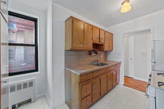 kitchen featuring radiator, light countertops, range with gas cooktop, a sink, and freestanding refrigerator
