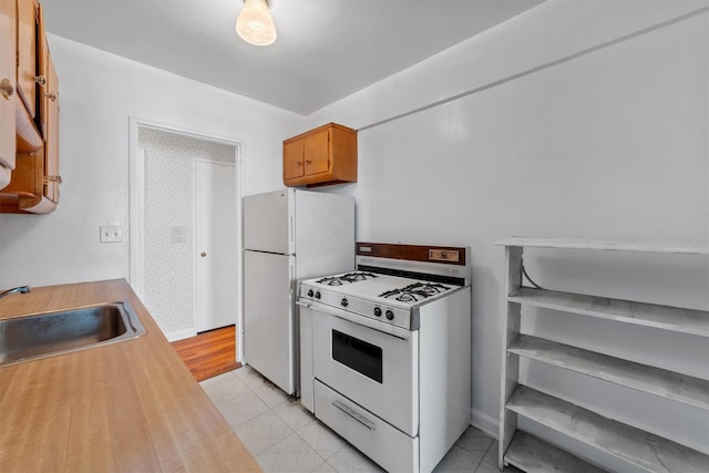 kitchen with brown cabinetry, white appliances, a sink, and light tile patterned flooring
