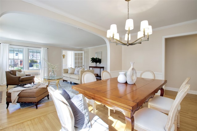 dining room with arched walkways, light wood-type flooring, crown molding, and an inviting chandelier