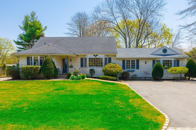 ranch-style home featuring roof with shingles and a front lawn