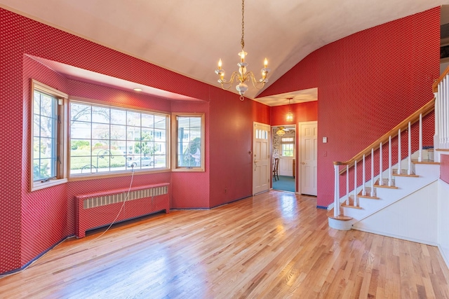 foyer entrance with radiator, an inviting chandelier, stairs, vaulted ceiling, and wood finished floors