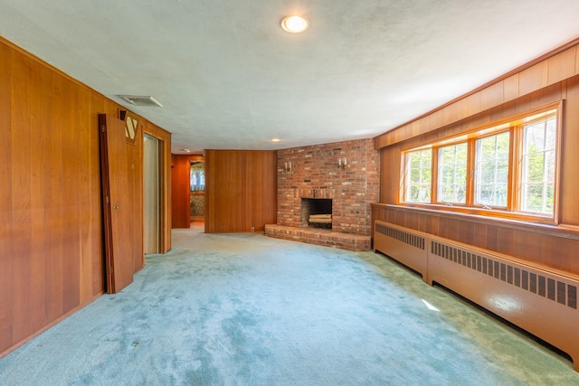 unfurnished living room with carpet floors, wood walls, radiator heating unit, a brick fireplace, and visible vents