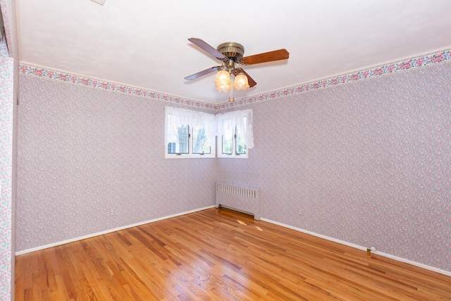 unfurnished room featuring wood finished floors, wallpapered walls, radiator, baseboards, and a ceiling fan