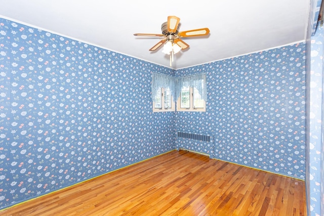 unfurnished room featuring wood finished floors, wallpapered walls, radiator, ceiling fan, and crown molding