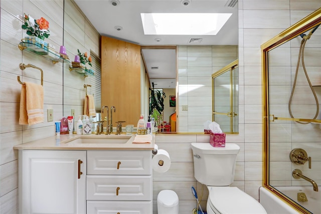 full bath featuring tile walls, vanity, bath / shower combo with glass door, toilet, and a skylight