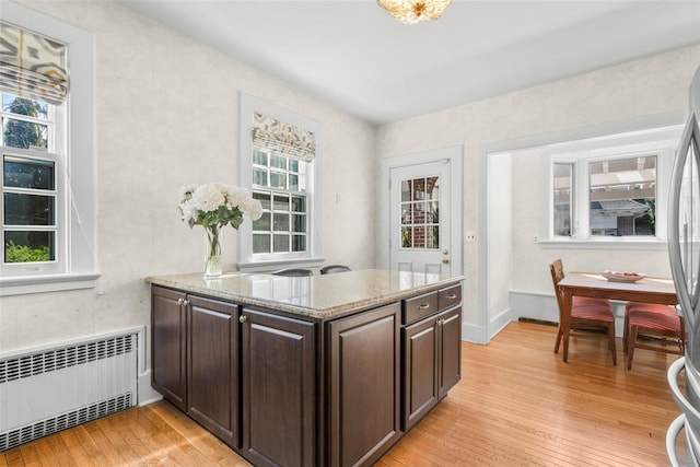 4610 Boston Post Rd, Pelham, NY 10803 - kitchen featuring radiator, light wood finished floors, dark brown cabinets, light stone countertops, and a peninsula