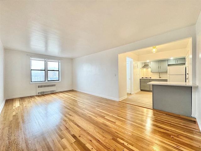 unfurnished living room with radiator heating unit, light wood finished floors, and baseboards