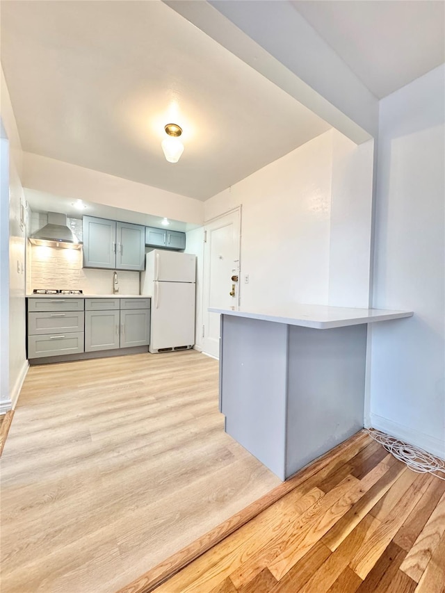 kitchen featuring freestanding refrigerator, wall chimney exhaust hood, light wood-style flooring, and stainless steel gas cooktop