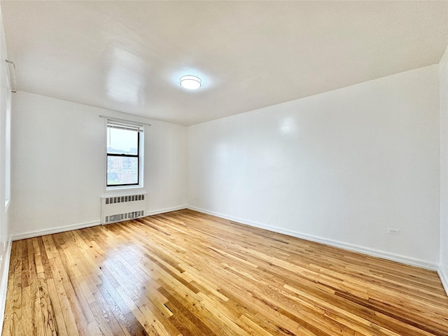 spare room featuring radiator, light wood-style floors, and baseboards