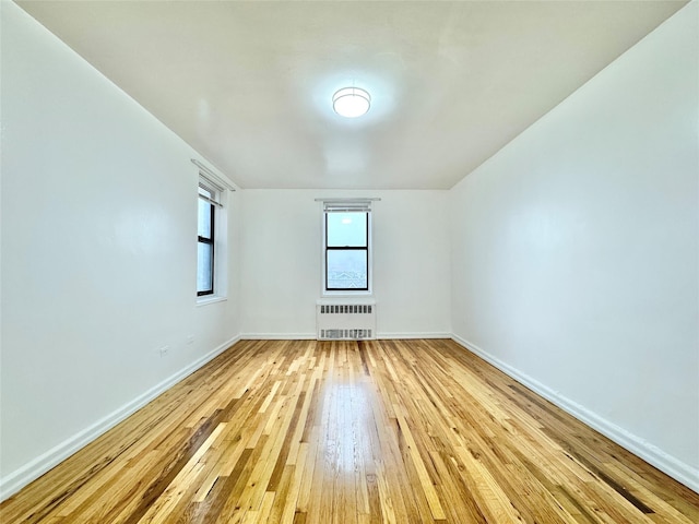spare room with radiator, light wood finished floors, and baseboards