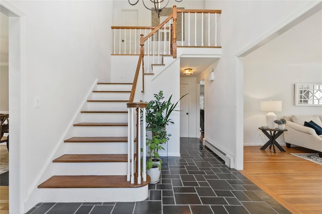 stairs with a baseboard heating unit, a high ceiling, and a chandelier