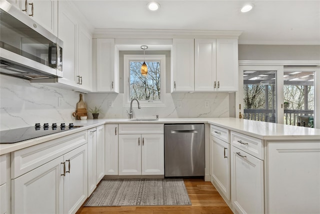 kitchen with a peninsula, appliances with stainless steel finishes, a sink, and white cabinetry
