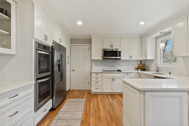 kitchen featuring white cabinets, a sink, light wood-style floors, light countertops, and appliances with stainless steel finishes