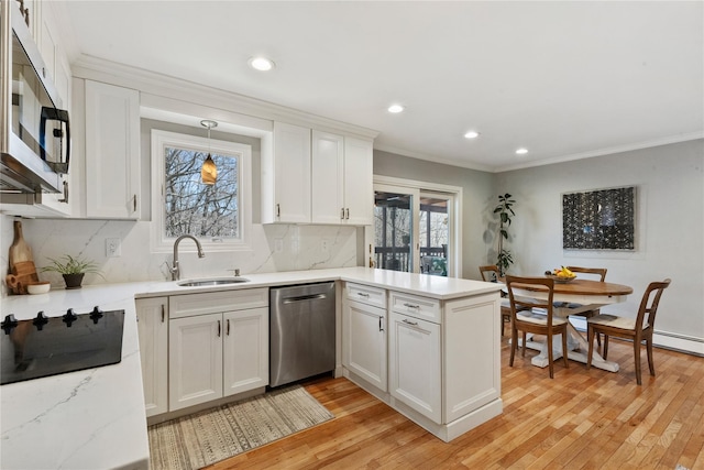 kitchen featuring white cabinets, a peninsula, light wood finished floors, a sink, and appliances with stainless steel finishes