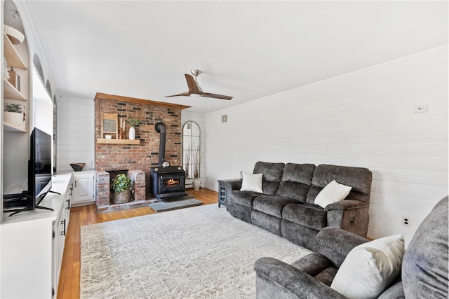 living area featuring light wood-style floors, ceiling fan, a wood stove, and ornamental molding