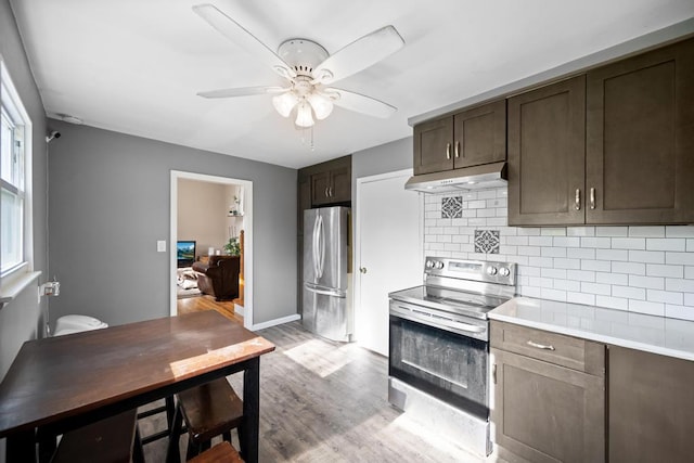 kitchen featuring stainless steel appliances, dark brown cabinets, under cabinet range hood, light wood-type flooring, and backsplash