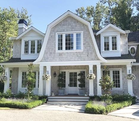 view of front of property featuring a gambrel roof, a chimney, and a porch
