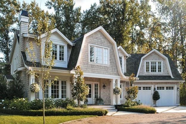 shingle-style home featuring concrete driveway, a gambrel roof, a shingled roof, and a chimney