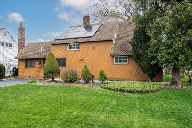 chalet / cabin featuring a front lawn, solar panels, roof with shingles, and a chimney