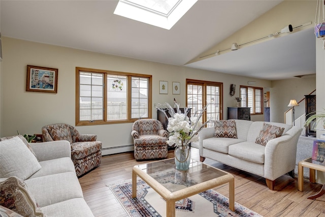 living area featuring vaulted ceiling with skylight, light wood-style floors, and baseboard heating