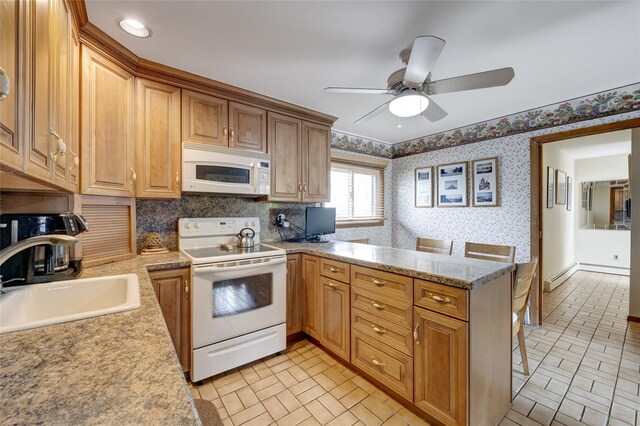 kitchen with a sink, wallpapered walls, white appliances, ceiling fan, and a peninsula