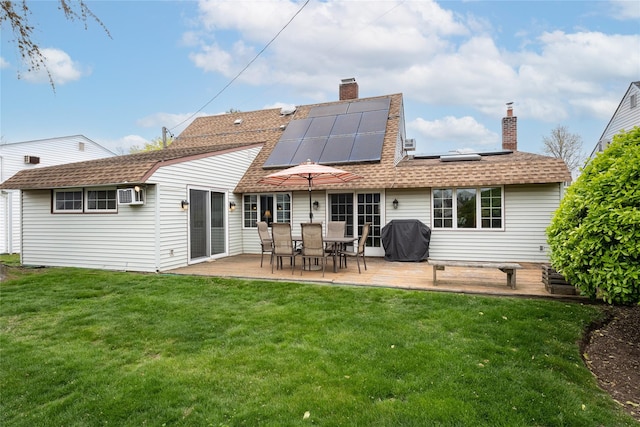 rear view of property featuring a patio area, a lawn, a chimney, a shingled roof, and solar panels