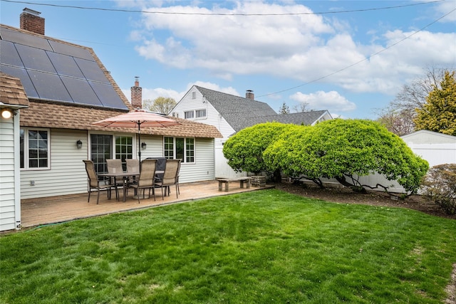 back of property with roof with shingles, a chimney, a lawn, roof mounted solar panels, and outdoor dining area
