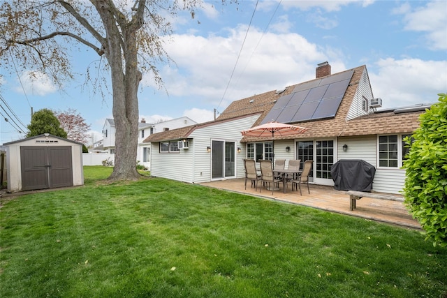 rear view of property with a shed, a lawn, an outdoor structure, solar panels, and roof with shingles