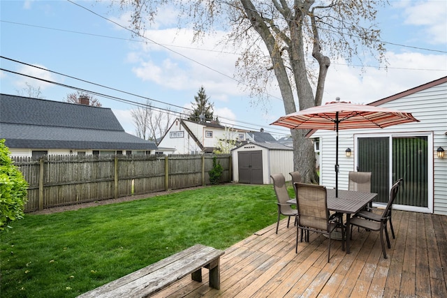 deck with a fenced backyard, an outdoor structure, outdoor dining area, a lawn, and a storage unit